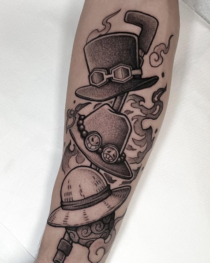 Tatouage blackwork des chapeaux d'Ace, Luffy et Sabo de One Piece, réalisé sur l'avant-bras.