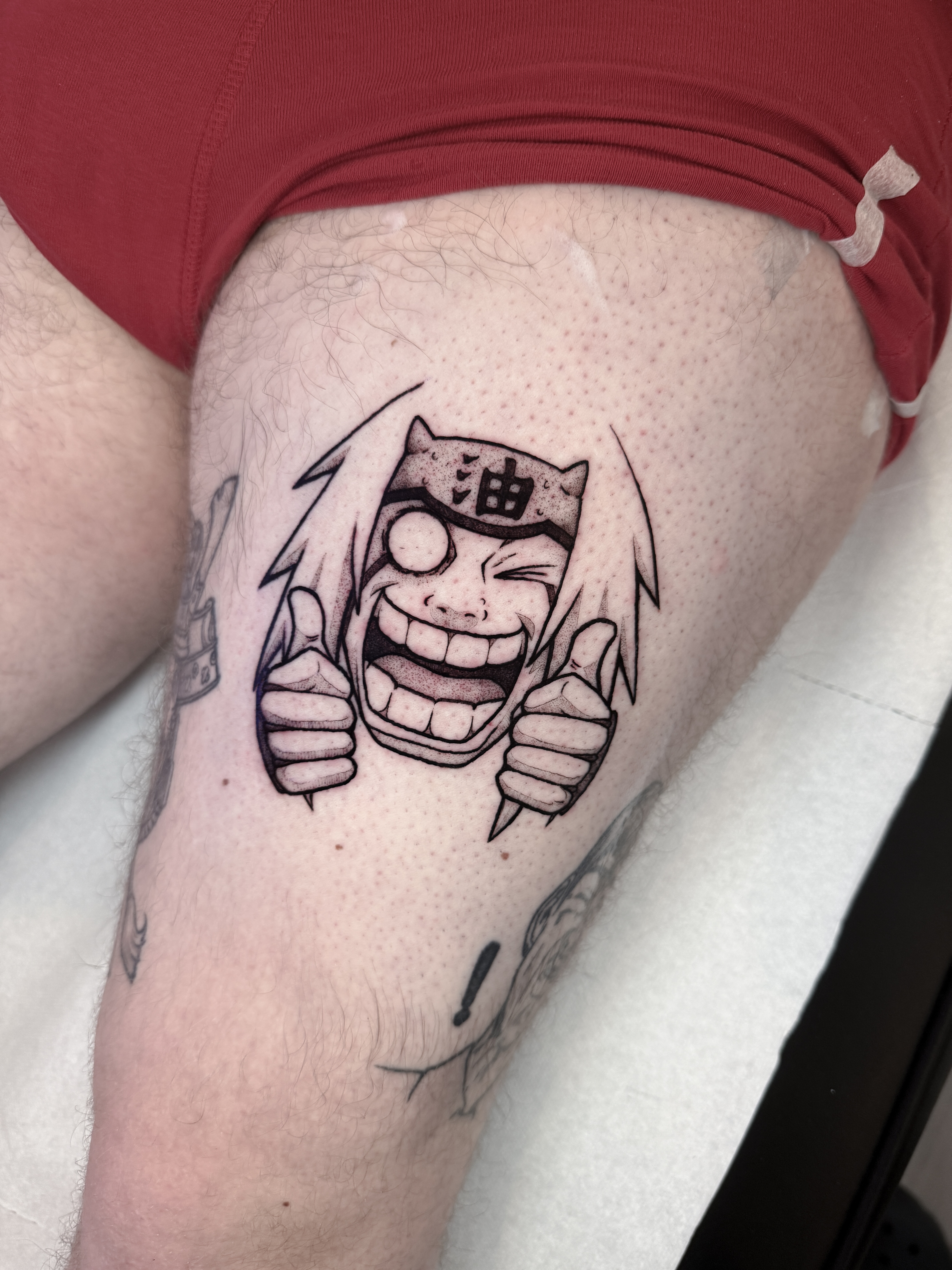 Tatouage blackwork de Jiraiya, personnage de Naruto, réalisé sur le devant de la cuisse avec lignes franches et forts contrastes.