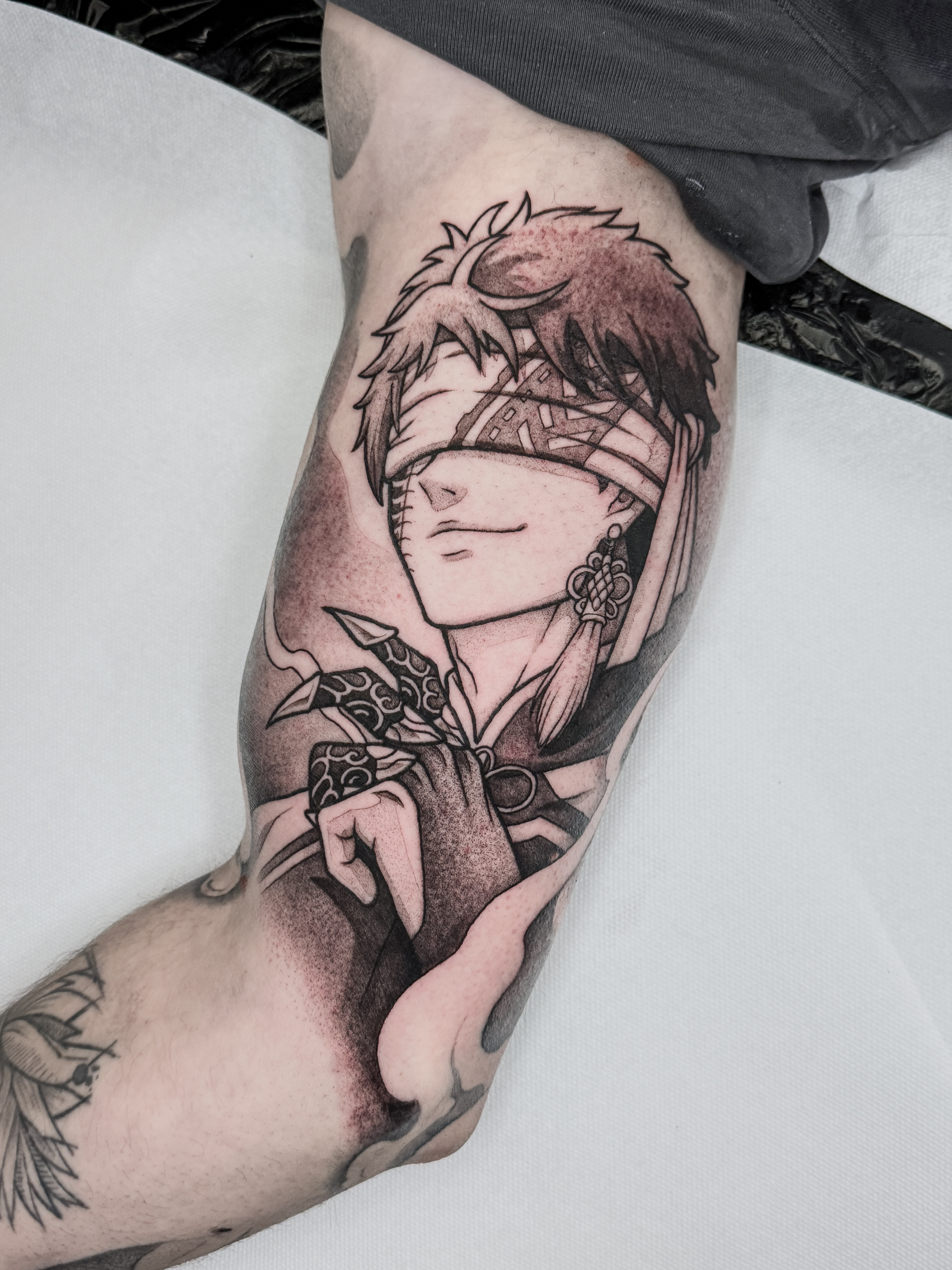 Tatouage blackwork de Qin Shi Huang, personnage de Valkyrie Apocalypse, réalisé à l'intérieur du biceps avec lignes marquées et forts contrastes.