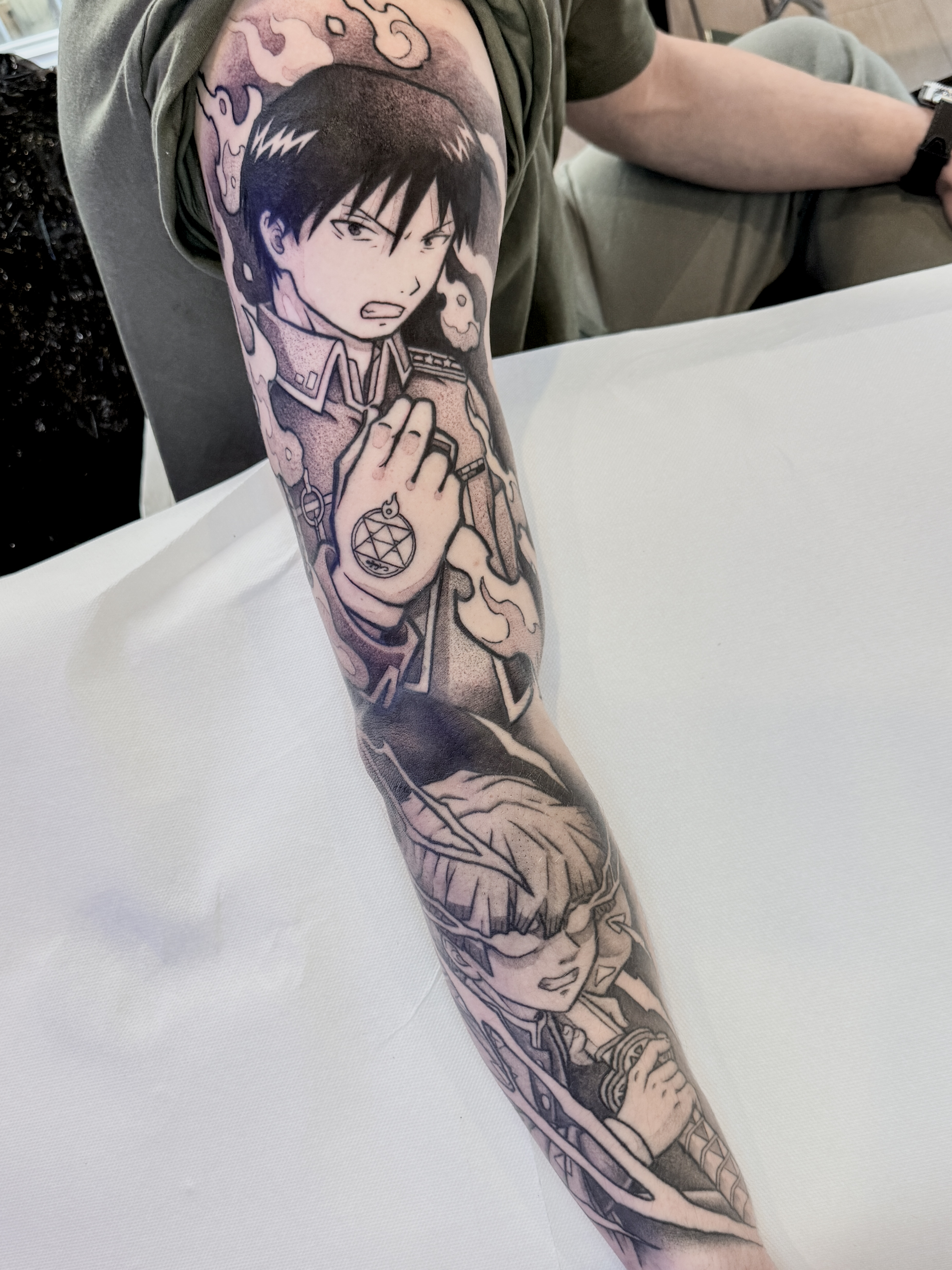 Sleeve blackwork de bras complet avec Zenitsu de Demon Slayer en bas et Roy Mustang de Fullmetal Alchemist en haut, représentés en combat.