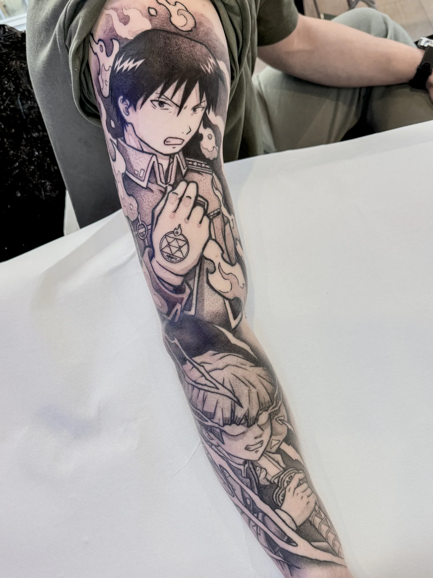 Sleeve blackwork de bras complet avec Zenitsu de Demon Slayer en bas et Roy Mustang de Fullmetal Alchemist en haut, représentés en combat.