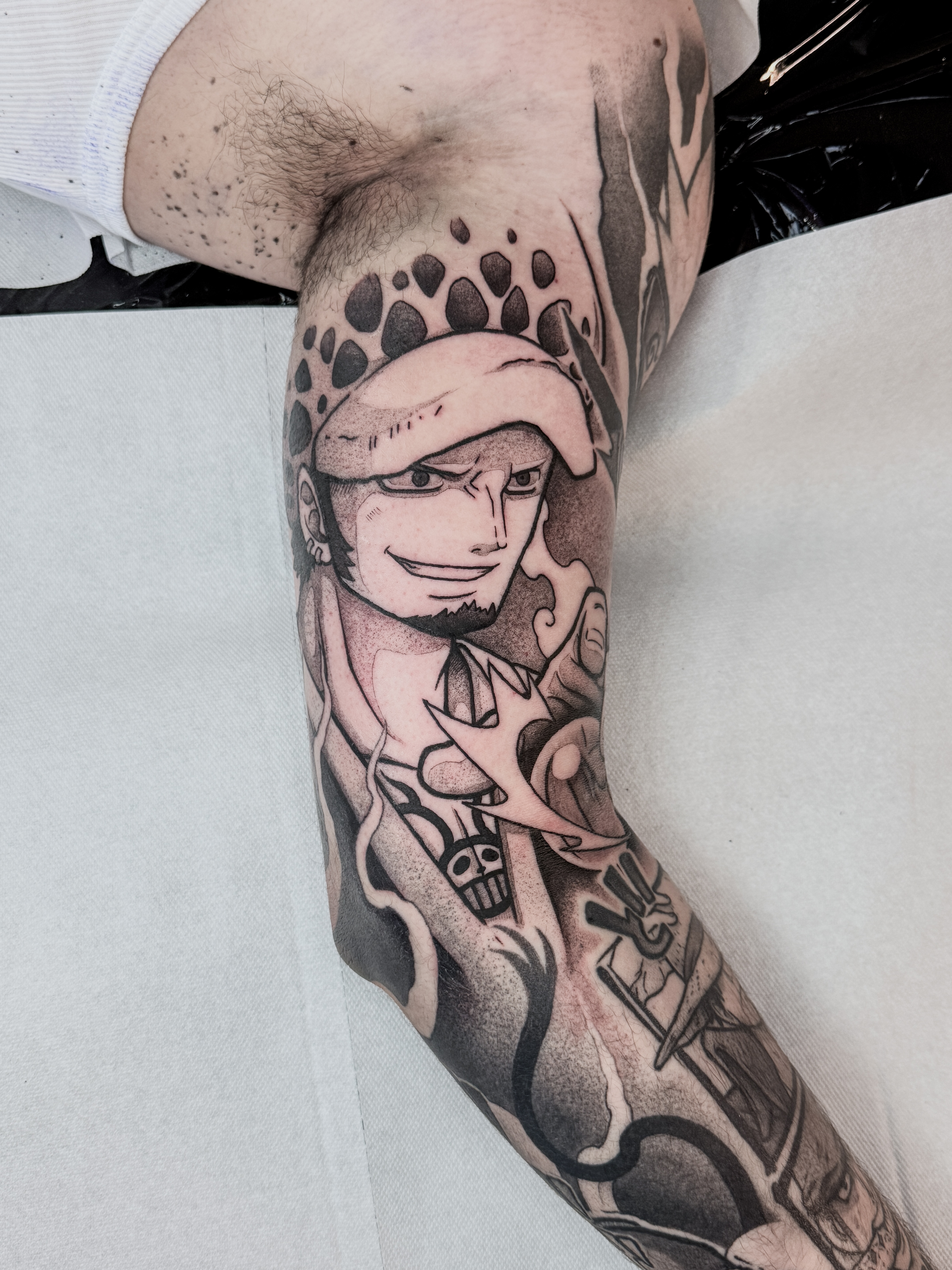 Tatouage blackwork contrasté de Trafalgar Law, personnage de One Piece, réalisé à l'intérieur du biceps pour compléter un bras complet Naruto et One Piece.